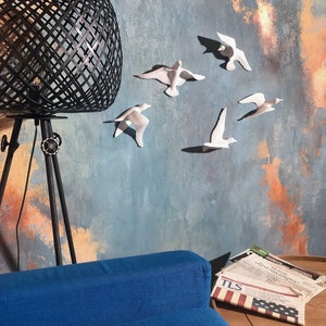 May include: A modern living room scene featuring a black geometric lamp, a blue sofa, and a wall adorned with white bird sculptures. The wall has a textured blue and orange painted design. Newspapers are on a wooden table.