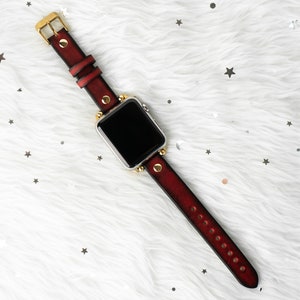 Puede incluir: Una correa de reloj de cuero rojo con detalles dorados y una esfera negra.