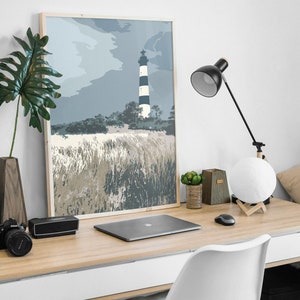 May include: A framed print of a black and white striped lighthouse on a grassy hill with a blue sky and clouds in the background.