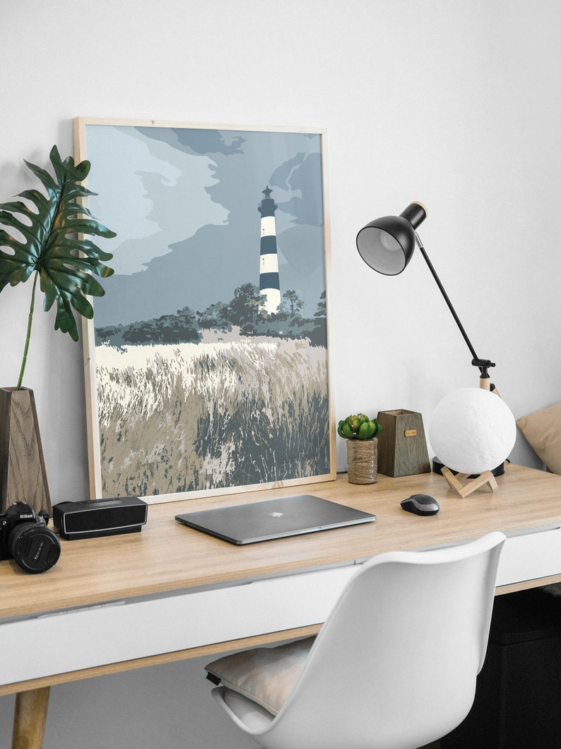 May include: A framed print of a black and white striped lighthouse on a grassy hill with a blue sky and clouds in the background.