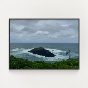 Pode incluir: Uma vista panorâmica de uma pequena ilha rochosa no oceano. A ilha é coberta de vegetação verde e cercada por ondas brancas. O céu está nublado e a água é de um azul profundo.