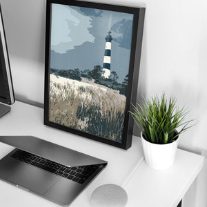 May include: A black framed print of a lighthouse with black and white stripes against a blue and gray cloudy sky. The lighthouse is surrounded by tall grass.