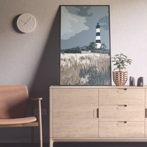 May include: A light wood cabinet with three drawers and a door. A framed print of a lighthouse with black and white stripes against a blue sky hangs above the cabinet. A brown chair sits to the left of the cabinet.