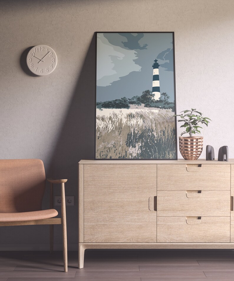 May include: A light wood cabinet with three drawers and a door. A framed print of a lighthouse with black and white stripes against a blue sky hangs above the cabinet. A brown chair sits to the left of the cabinet.
