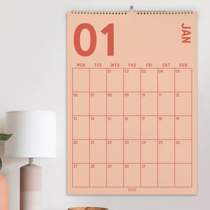 May include: A wall calendar for January 2025, featuring a salmon-colored background with red grid lines and numerals. The calendar displays the days of the week and dates from 01 to 31. The word "JAN" is printed vertically on the right side.