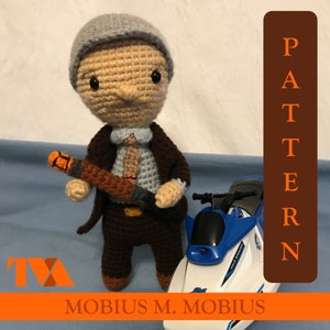 May include: Crocheted amigurumi doll of a man wearing a brown suit, a blue shirt, and a gray hat. He is holding a brown and orange object in his right hand. The doll is standing next to a blue and white toy jet ski.