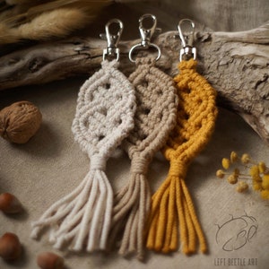 Peut inclure: Trois porte-clés en macramé avec des glands de couleur beige, marron et jaune. Les porte-clés ont la forme d'une feuille et sont munis d'un anneau en métal argenté.