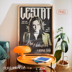 May include: A framed poster with the title "LESTAT" in bold white letters against a black background. The poster features an image of a person with long hair and the text "The Vampire World Tour." An orange lamp and a plant are in the foreground.