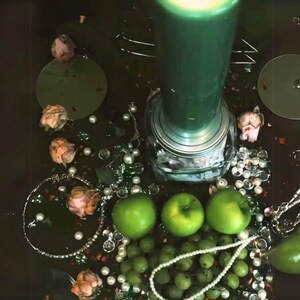 Peut inclure: Une bougie verte avec une base argent&eacute;e repose sur une surface sombre entour&eacute;e de pommes vertes, de perles blanches et de roses roses.
