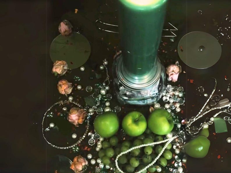 Peut inclure: Une bougie verte avec une base argent&eacute;e repose sur une surface sombre entour&eacute;e de pommes vertes, de perles blanches et de roses roses.