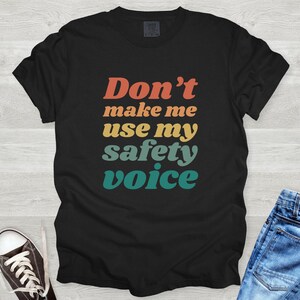 May include: Black t-shirt with a retro-style graphic that says "Don't make me use my safety voice".