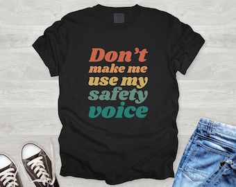 May include: Black t-shirt with a retro-style graphic that says "Don't make me use my safety voice".