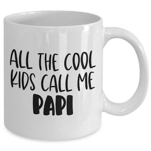 May include: White ceramic mug with a curved handle. The mug features the text "ALL THE COOL KIDS CALL ME PAPI" in black, bold, handwritten-style lettering. The mug is designed for hot or cold beverages.
