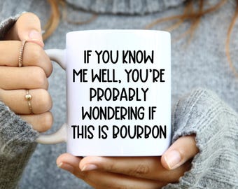Può includere: Una tazza in ceramica bianca con il testo stampato in nero: IF YOU KNOW ME WELL, YOU'RE PROBABLY WONDERING IF THIS IS BOURBON. La tazza ha una finitura liscia e un manico curvo, offrendo una visione chiara del carattere nero in grassetto.