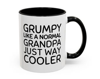 Może przedstawiać: Biały ceramiczny kubek z czarnym wnętrzem i czarnym uchwytem. Na zewnątrz znajduje się czarny napis: GRUMPY LIKE A NORMAL GRANDPA JUST WAY COOLER. Kubek ma cylindryczny kształt i gładkie wykończenie, prezentując wyraźne, pogrubione litery.