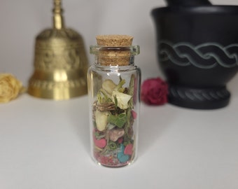 May include: A small glass bottle with a cork stopper filled with dried herbs, flowers, and colorful beads. The bottle is clear and the contents are visible.
