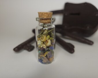 May include: A small glass bottle with a cork stopper filled with dried flowers and blue and green stones. The bottle is sitting on a white surface with a brown padlock and keys in the background.