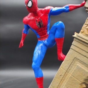 Pu&ograve; includere: Una action figure rossa e blu di Spider-Man in una posa dinamica, che scala un muro di pietra. La figura &egrave; dettagliata con un logo a forma di ragno sul petto.