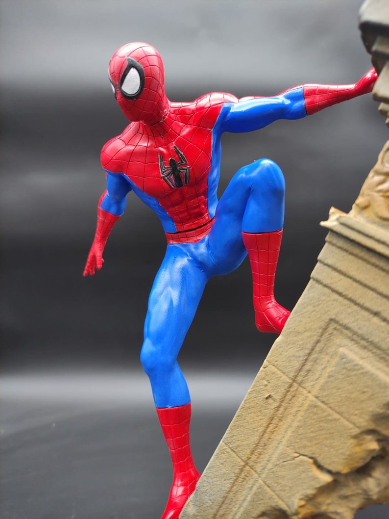 Pu&ograve; includere: Una action figure rossa e blu di Spider-Man in una posa dinamica, che scala un muro di pietra. La figura &egrave; dettagliata con un logo a forma di ragno sul petto.