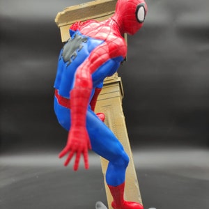 Pu&ograve; includere: Una action figure rossa e blu di Spider-Man che scala un muro. La figura &egrave; in posa in una posa d'azione dinamica con una gamba sollevata e l'altra piantata sul muro. La figura &egrave; in plastica e ha una verniciatura dettagliata.