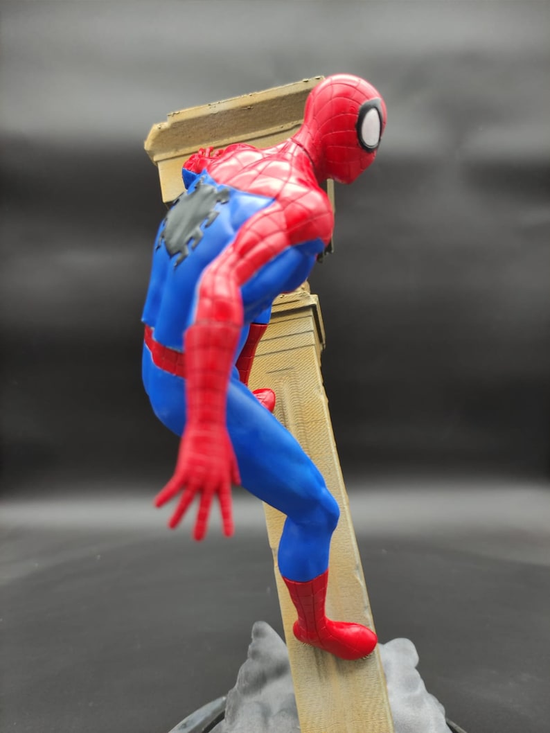 Pu&ograve; includere: Una action figure rossa e blu di Spider-Man che scala un muro. La figura &egrave; in posa in una posa d'azione dinamica con una gamba sollevata e l'altra piantata sul muro. La figura &egrave; in plastica e ha una verniciatura dettagliata.