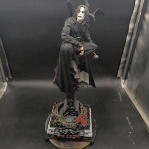 Può includere: Statuetta dettagliata di un personaggio del film "Il Corvo". La figura è vestita di nero, con trucco bianco e una rosa. La base presenta il titolo del film e rose rosse.