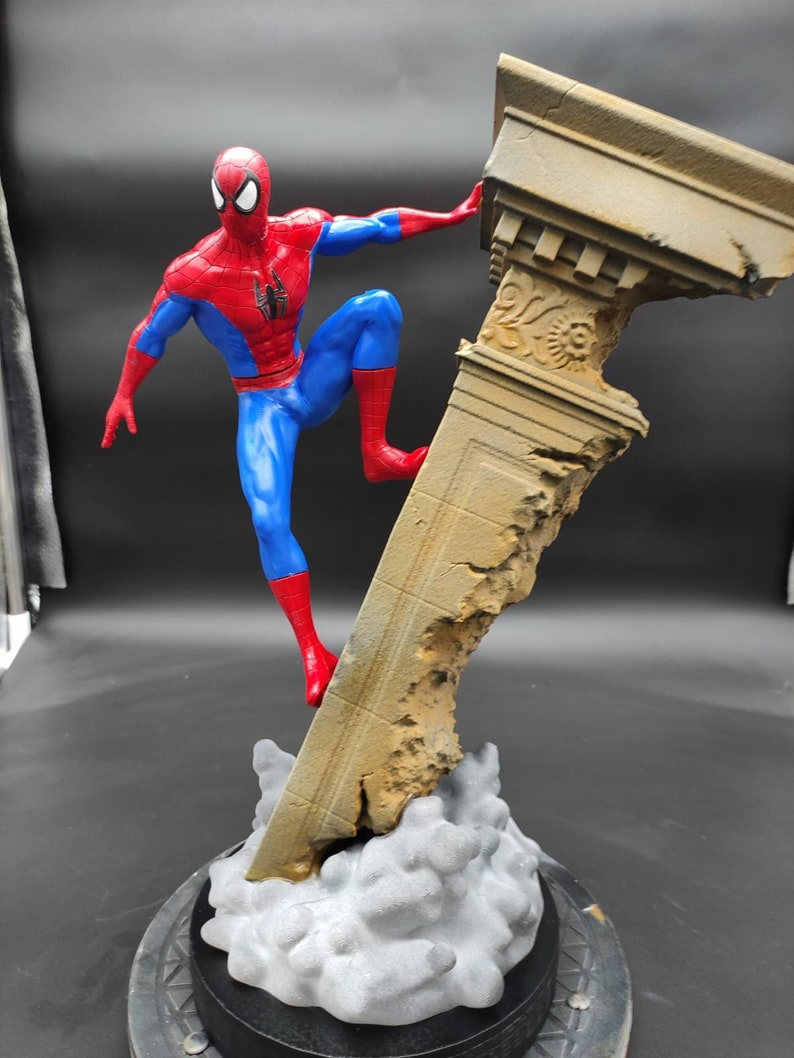 Pu&ograve; includere: Una action figure di Spider-Man rossa e blu &egrave; in posa mentre scala una colonna di pietra rotta. La figura &egrave; posizionata su uno sfondo grigio. La colonna &egrave; rotta e ha una texture ruvida. La figura &egrave; in piedi su una base a forma di nuvola.