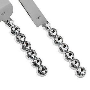 May include: A silver cake knife and server set with crystal-like embellishments. The server is engraved with the text "Sean & Amanda June 18, 2020".