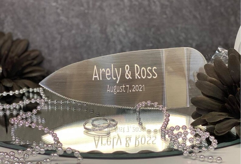 May include: Silver cake server with a serrated edge, engraved with the names "Arely & Ross" and the date "August 7, 2021".