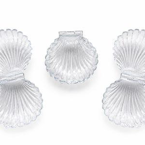 May include: Three clear, transparent plastic containers shaped like seashells. Two of the containers are open and elongated, featuring a hinged design with ribbed textures. The third container is a single, rounded shell-shaped piece.