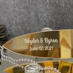K&ouml;nnte beinhalten: Ein goldfarbener Kuchenspachtel mit der Aufschrift "Skylar & Byron June 12, 2021".
