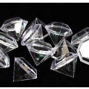May include: A cluster of clear, faceted diamond-shaped boxes against a black backdrop. The boxes, with multiple sides, reflect light, producing a sparkling effect. The shapes vary, with some appearing as complete diamonds and others as open-topped containers.