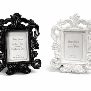 Puede incluir: Dos marcos de fotos ornamentados, uno negro y otro blanco, con detalles de volutas. Cada marco tiene una abertura rectangular con el texto "Photo Frame, Cadre Photo, Cuadro de Foto". El marco negro mide 4,45 cm x 6,35 cm.