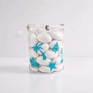 May include: A transparent, cylindrical container filled with white, oval sweets. The container features blue tropical-themed designs, such as palm trees, a lighthouse, and a starfish. A white drawstring closure is at the top.