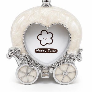 May include: A carriage-shaped photo frame with a pearlescent white finish and silver-toned metal accents. The frame features a heart-shaped opening bordered by silver beads, with a small flower icon and the text Happy Time printed inside.