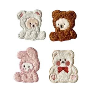 May include: Four embroidered iron-on patches featuring cute cartoon animals. The patches are white, brown, pink, and white with a red bow. The animals are a bear, a bear, a bunny, and a bear.