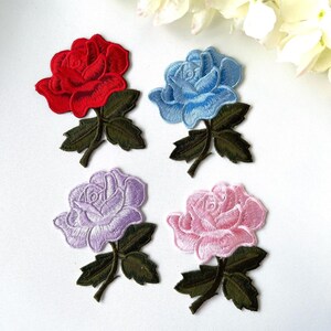 May include: Four embroidered iron-on patches featuring roses in red, blue, purple, and pink. Each rose has green leaves and a stem.