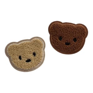 May include: Two bear-shaped patches with a textured, fuzzy surface. One patch is light tan with a darker tan border, and the other is dark brown with a matching dark brown border. Both feature simple black embroidered eyes and a nose.