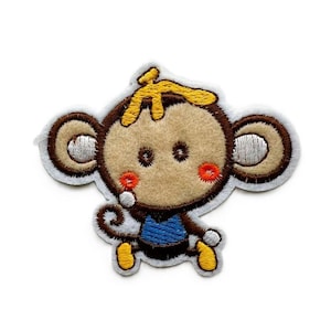 May include: An embroidered iron-on patch featuring a cartoon monkey with a tan face, brown ears, and a yellow tuft of hair. The monkey wears a blue shirt and has small red cheeks, with white, brown, and yellow thread detailing on a white background.