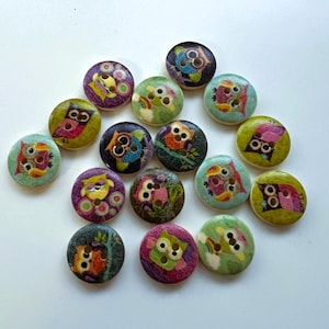 May include: A collection of wooden buttons with owl designs. The buttons are round and feature colorful owl illustrations in various colors, including green, purple, and orange. Each button has two or four holes for sewing.