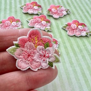 May include: Six pink embroidered flower patches with green leaves. The patches are on a green and white striped background.