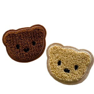 May include: Two fuzzy brown and beige bear face patches with embroidered black eyes and noses.