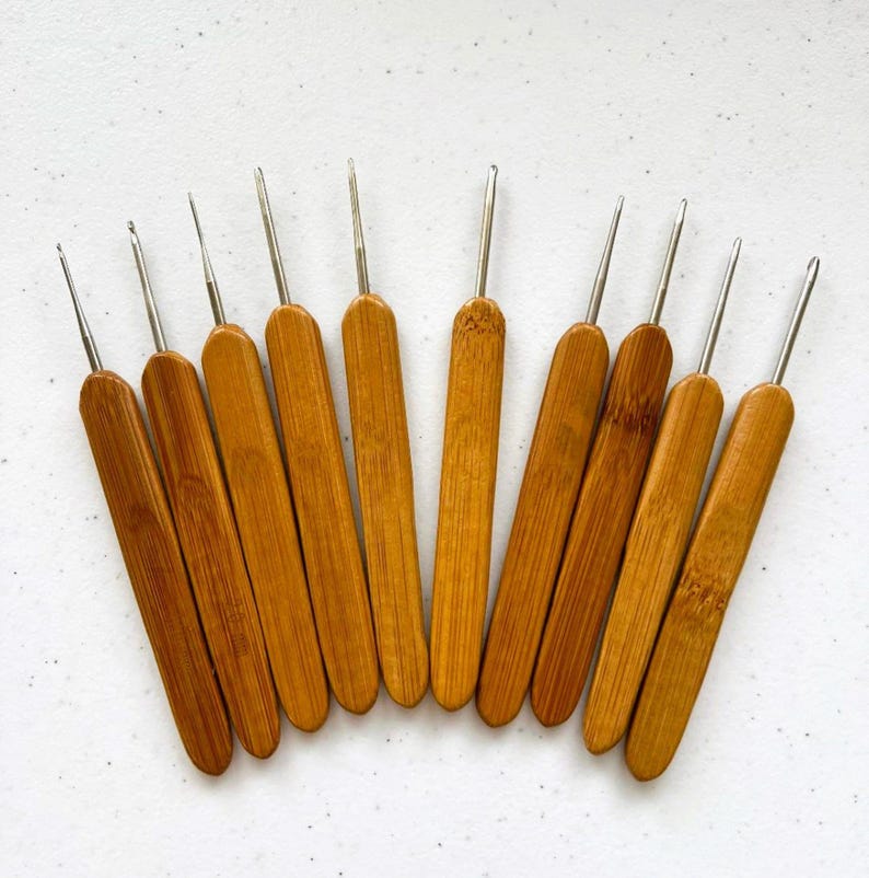 May include: Set of 10 bamboo crochet hooks with silver tips. The hooks are arranged in a fan shape, with the smallest hook at the top and the largest hook at the bottom.