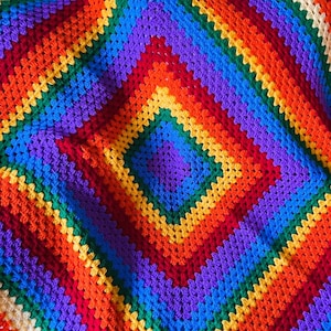 May include: A rainbow crochet blanket with a diamond pattern. The blanket is made with different shades of red, orange, yellow, green, blue, purple, and white yarn.