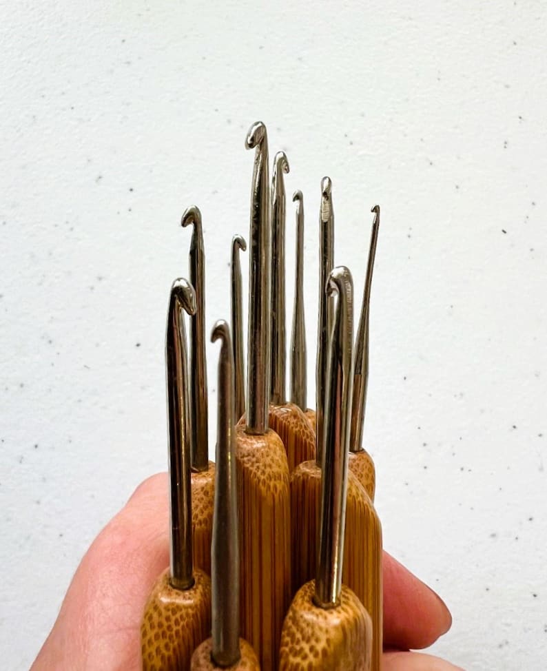 May include: A set of 12 bamboo crochet hooks with silver metal hooks. The hooks are arranged in a fan shape, with the largest hook at the top and the smallest hook at the bottom.