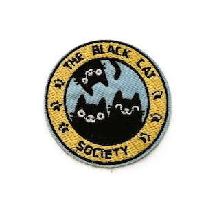 Peut inclure: Un écusson brodé circulaire présentant un centre bleu clair avec trois silhouettes de chats noirs. Une bordure jaune entoure le centre, contenant le texte brodé noir THE BLACK CAT SOCIETY et de petites icônes d'empreintes de pattes.