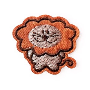 May include: Embroidered patch featuring a cartoon lion with an orange mane and a light brown face. The lion's face is detailed with embroidered features, including a nose, whiskers, and eyes. The patch has a scalloped edge.