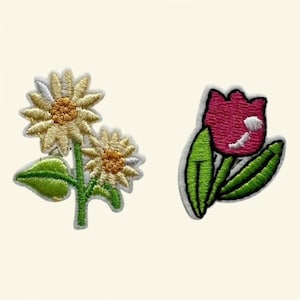 May include: Two embroidered fabric patches. One patch features two light yellow daisies with orange centers and green leaves. The second patch depicts a single magenta tulip with a white accent and two green leaves on a white background.
