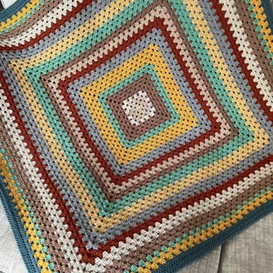 May include: A crocheted blanket with a square pattern in shades of blue, green, yellow, brown, and red. The blanket has a blue border.
