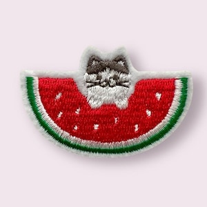 May include: Embroidered iron-on patch featuring a cartoon cat wearing a watermelon slice as a hat. The cat is white with gray ears and a black nose. The watermelon is red with black seeds and a green rind.